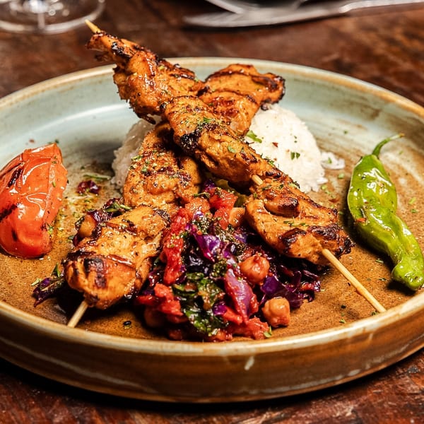Grilled chicken skewers with rice, roasted tomato, green pepper, and a colorful vegetable medley.