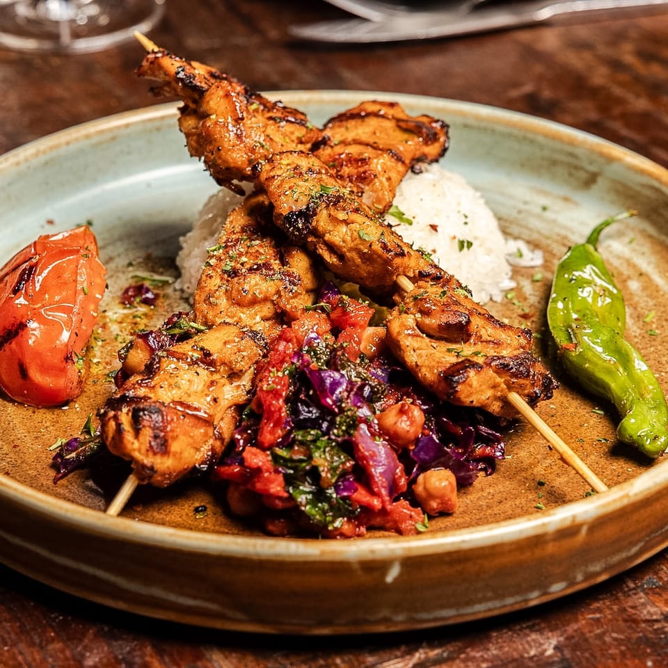 Grilled chicken skewers with rice, roasted tomato, green pepper, and a colorful vegetable medley.